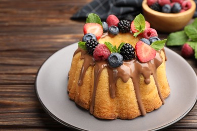 Photo of Tasty Bundt cake with berries, chocolate and mint on wooden table, closeup