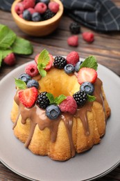 Photo of Tasty Bundt cake with berries, chocolate and mint on wooden table, closeup
