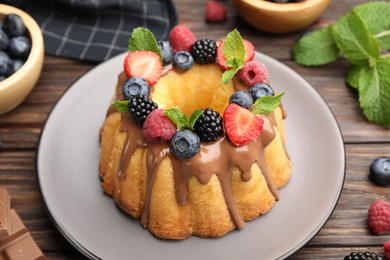 Photo of Tasty Bundt cake with berries, chocolate and mint on wooden table, closeup