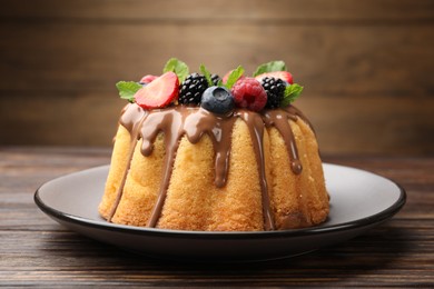 Photo of Tasty Bundt cake with berries, chocolate and mint on wooden table, closeup