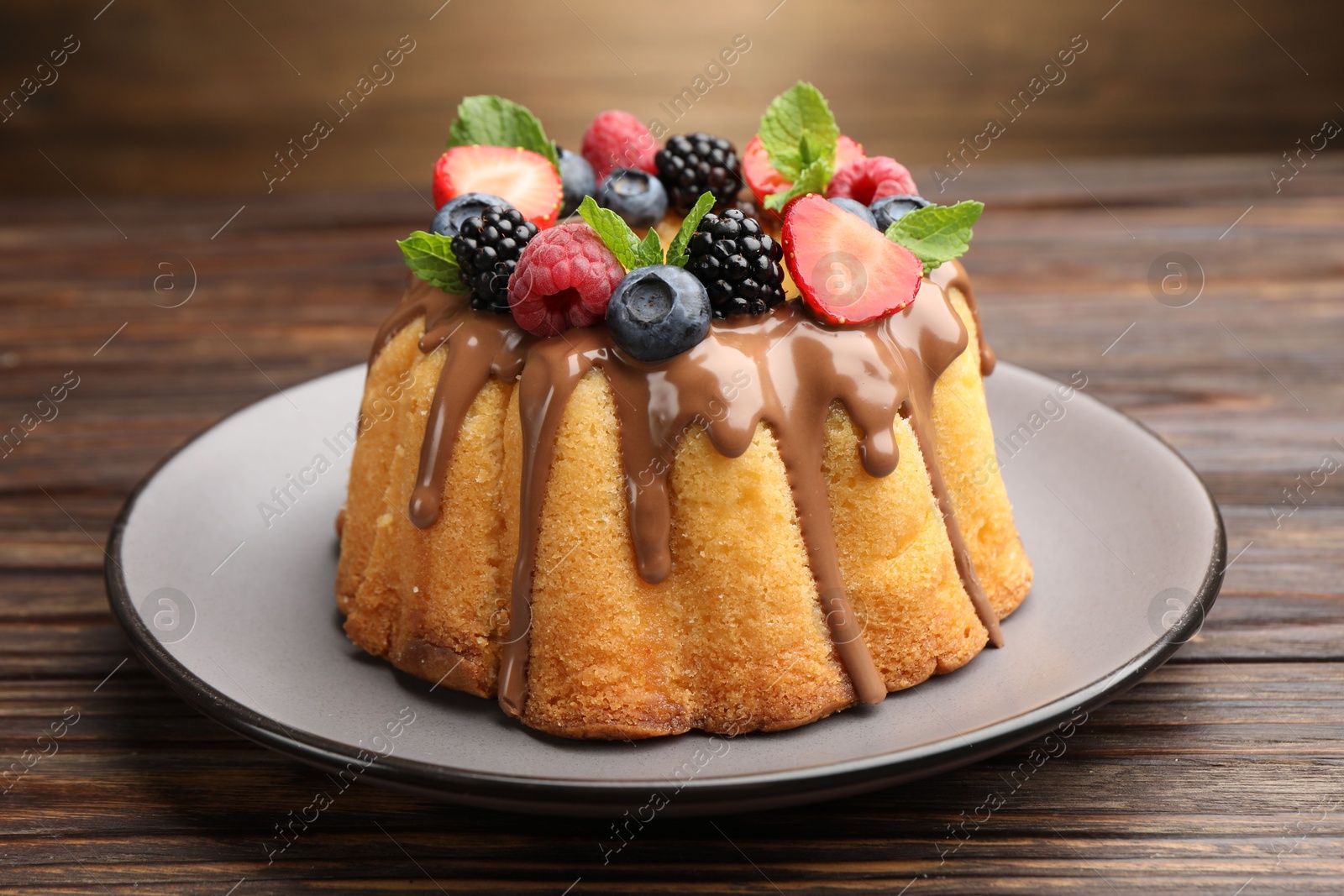 Tasty Bundt cake with berries, chocolate and mint on wooden table, closeup Photo of Tasty Bundt cake with berries, chocolate and mint on wooden table, closeup