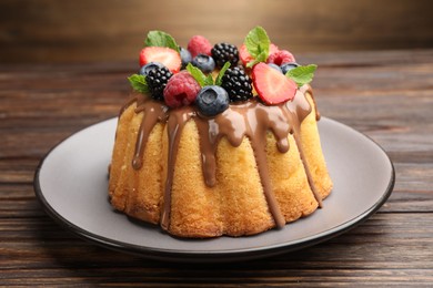 Photo of Tasty Bundt cake with berries, chocolate and mint on wooden table, closeup