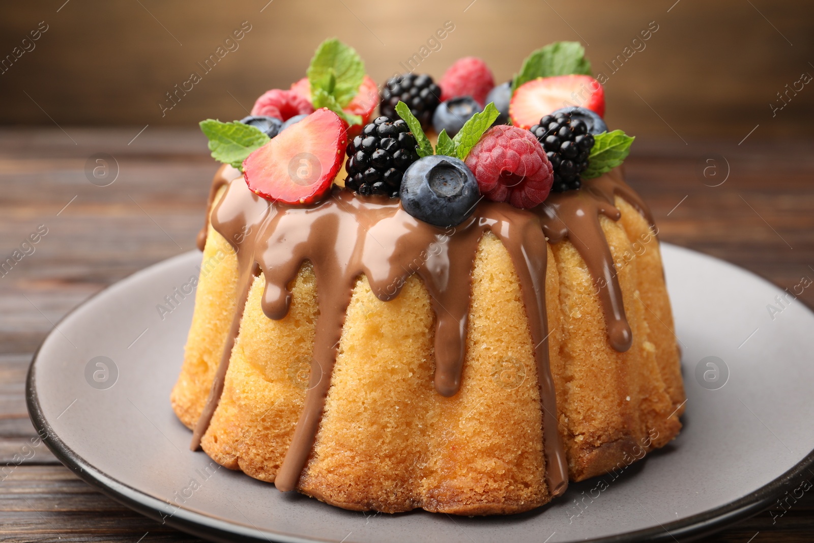 Photo of Tasty Bundt cake with berries, chocolate and mint on wooden table, closeup