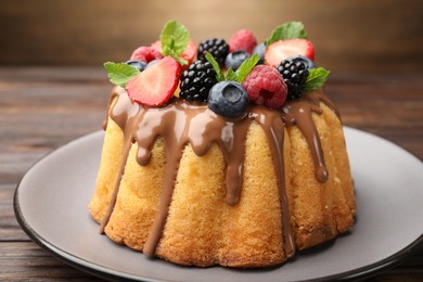 Photo of Tasty Bundt cake with berries, chocolate and mint on wooden table, closeup