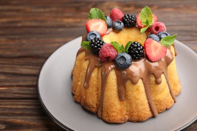 Photo of Tasty Bundt cake with berries, chocolate and mint on wooden table, closeup