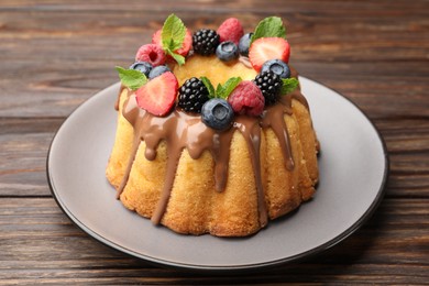 Photo of Tasty Bundt cake with berries, chocolate and mint on wooden table, closeup