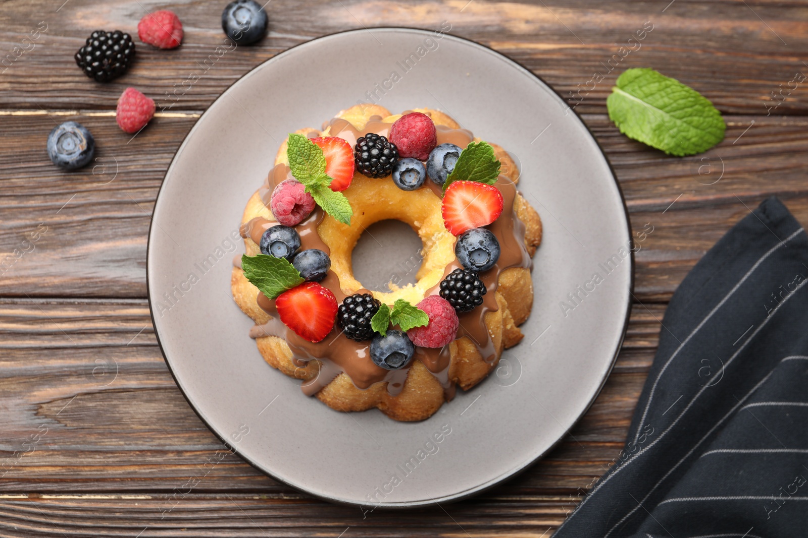 Tasty Bundt cake with berries, chocolate and mint on wooden table, top view Photo of Tasty Bundt cake with berries, chocolate and mint on wooden table, top view