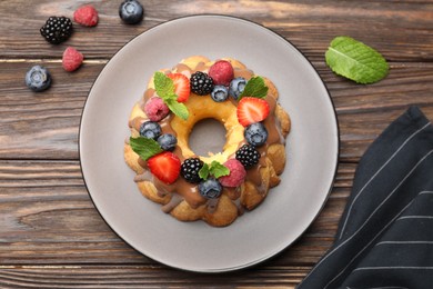 Photo of Tasty Bundt cake with berries, chocolate and mint on wooden table, top view