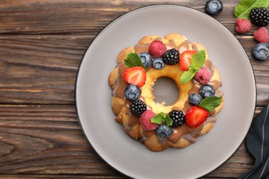 Photo of Tasty Bundt cake with berries, chocolate and mint on wooden table, top view. Space for text