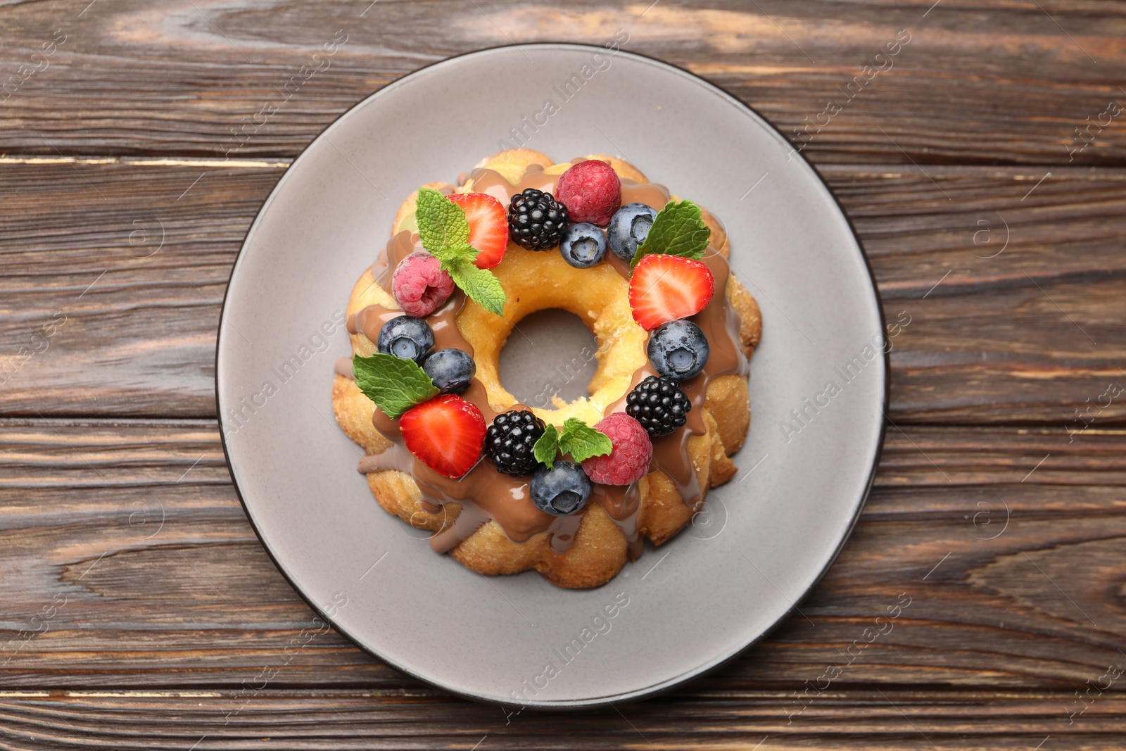 Photo of Tasty Bundt cake with berries, chocolate and mint on wooden table, top view