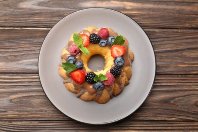 Photo of Tasty Bundt cake with berries, chocolate and mint on wooden table, top view