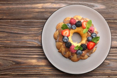 Photo of Tasty Bundt cake with berries, chocolate and mint on wooden table, top view. Space for text