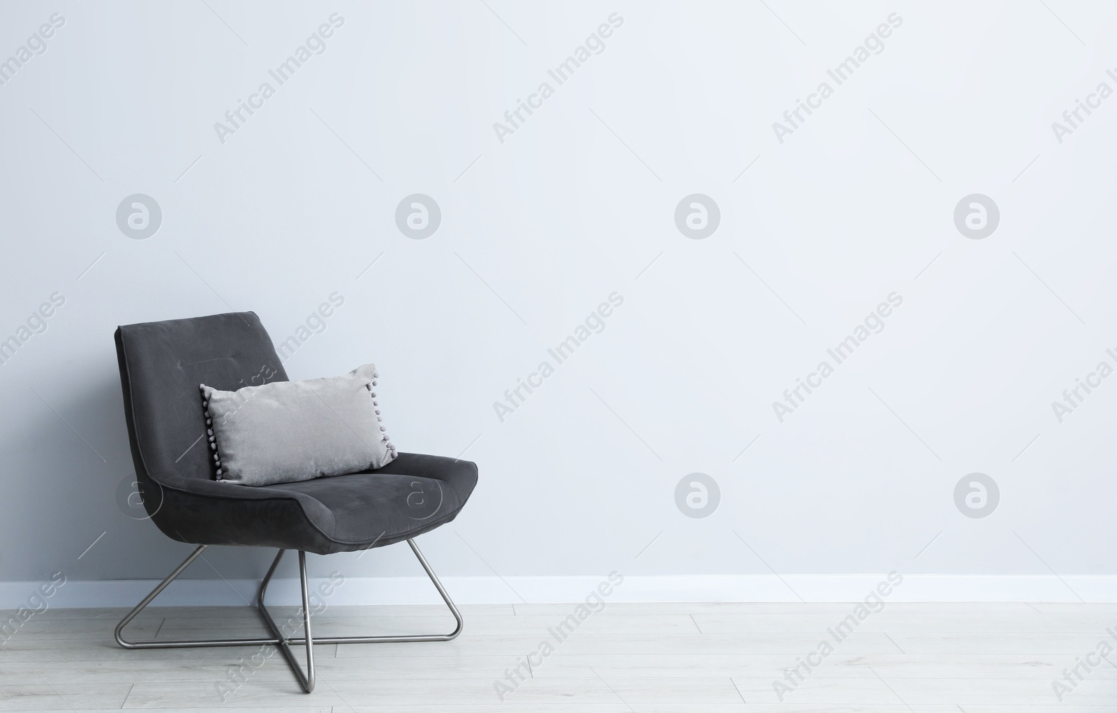 Photo of Comfortable armchair and cushion near light gray wall indoors. Space for text