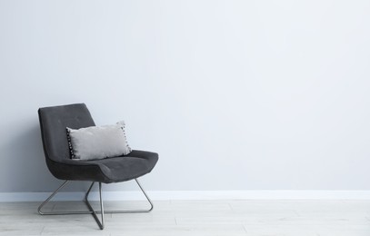 Photo of Comfortable armchair and cushion near light gray wall indoors. Space for text