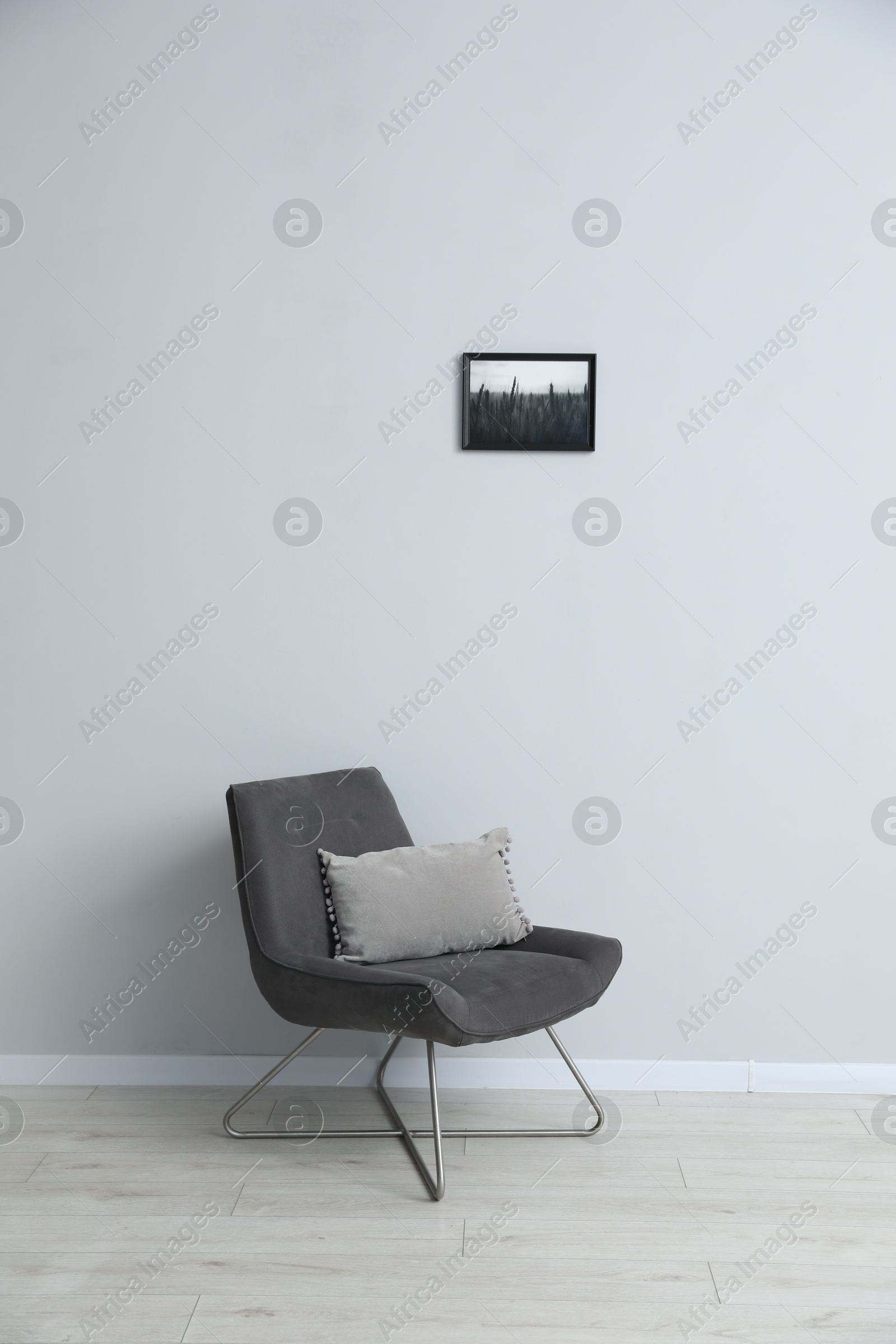 Photo of Comfortable armchair and cushion near light gray wall indoors