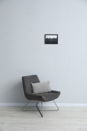 Photo of Comfortable armchair and cushion near light gray wall indoors