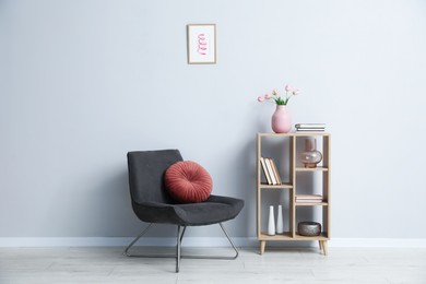 Photo of Comfortable armchair and wooden rack with different decor near light gray wall indoors