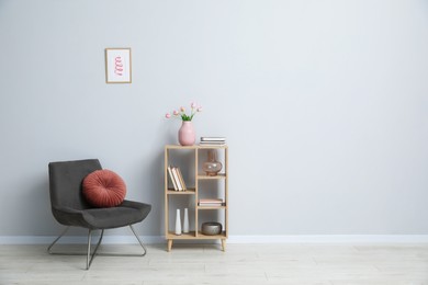 Photo of Comfortable armchair and wooden rack with different decor near light gray wall indoors. Space for text