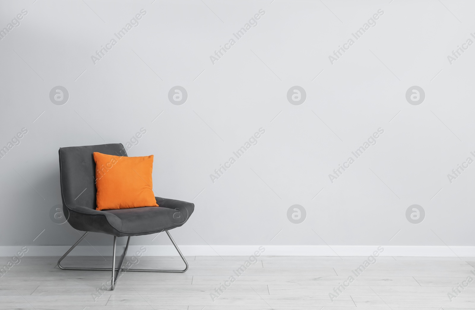 Comfortable armchair and orange cushion near light gray wall indoors. Space for text Photo of Comfortable armchair and orange cushion near light gray wall indoors. Space for text