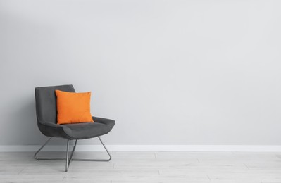 Photo of Comfortable armchair and orange cushion near light gray wall indoors. Space for text