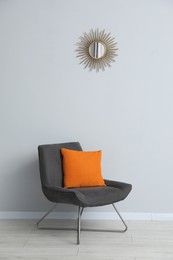 Photo of Comfortable armchair and orange cushion near light gray wall indoors
