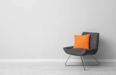 Photo of Comfortable armchair and orange cushion near light gray wall indoors. Space for text