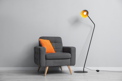 Photo of Comfortable armchair and lamp near light gray wall indoors