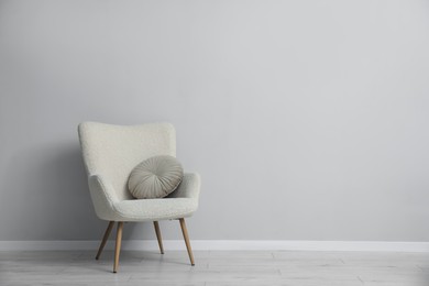 Photo of Comfortable armchair and cushion near light gray wall indoors. Space for text