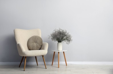 Photo of Comfortable armchair and vase with flowers near light gray wall indoors. Space for text
