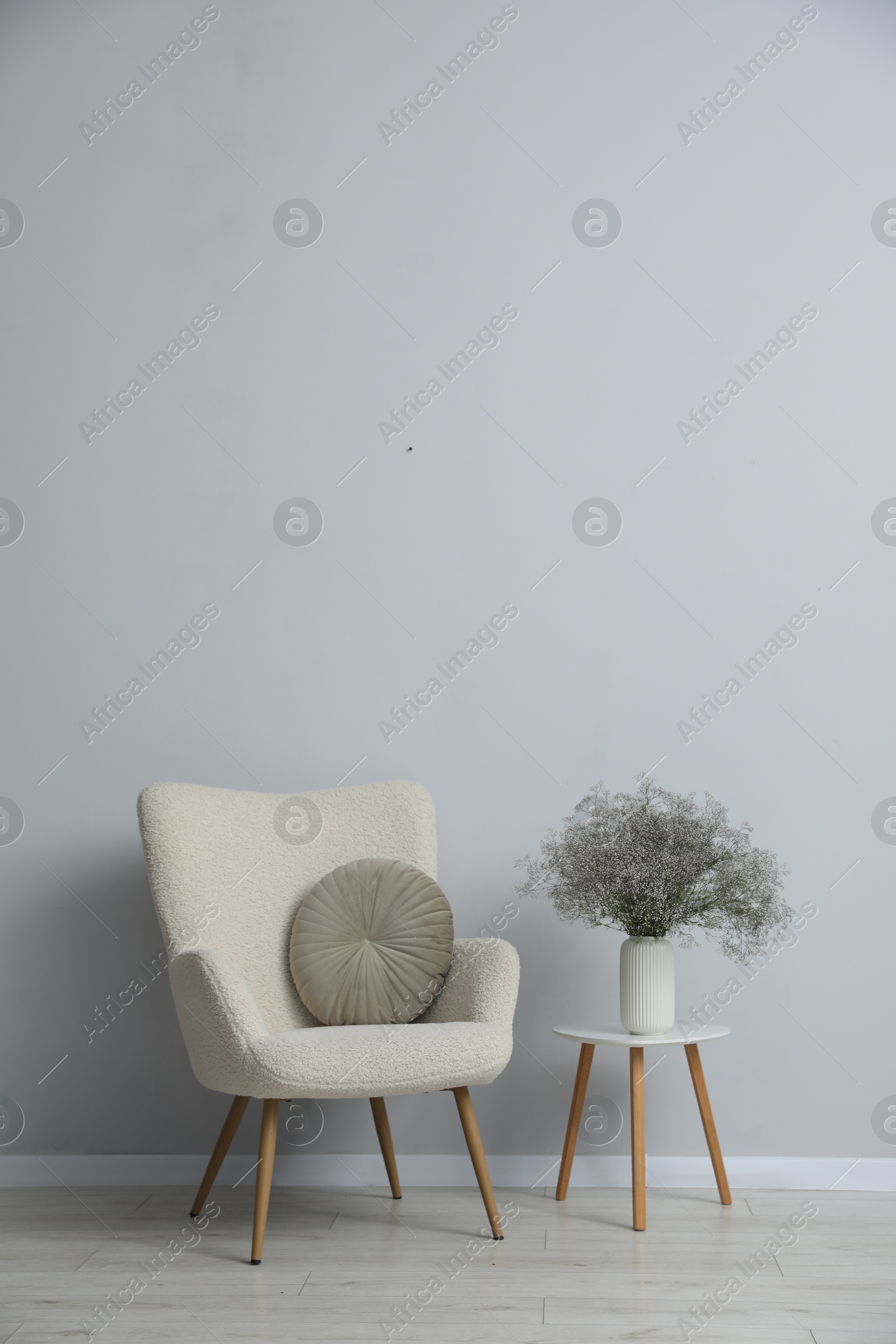 Comfortable armchair and vase with flowers near light gray wall indoors Photo of Comfortable armchair and vase with flowers near light gray wall indoors