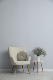Photo of Comfortable armchair and vase with flowers near light gray wall indoors