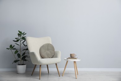 Photo of Comfortable armchair, houseplant, books and cup near light gray wall indoors