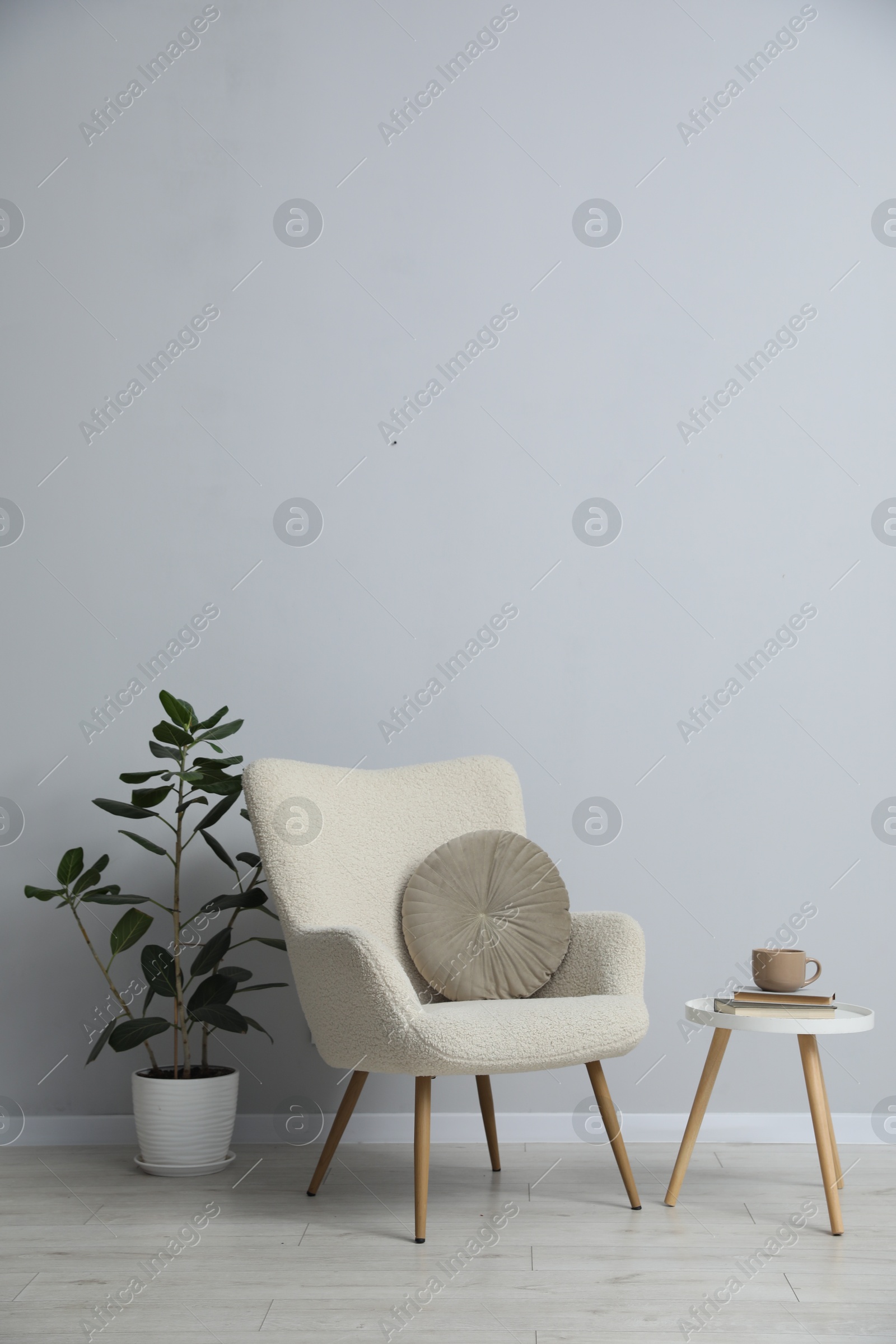Photo of Comfortable armchair, houseplant, books and cup near light gray wall indoors
