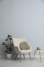 Photo of Comfortable armchair, houseplant, books and cup near light gray wall indoors