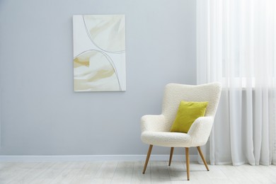 Photo of Comfortable armchair and cushion near light gray wall indoors
