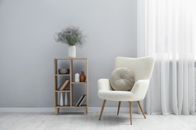 Photo of Comfortable armchair and wooden rack with different decor near light gray wall indoors