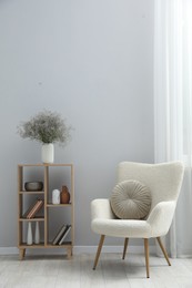 Photo of Comfortable armchair and wooden rack with different decor near light gray wall indoors