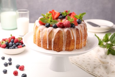 Photo of Delicious bundt cake with berries, glaze and mint on white table against grey background, closeup