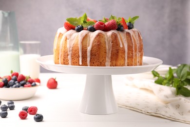Photo of Delicious bundt cake with berries, glaze and mint on white wooden table against grey background, closeup