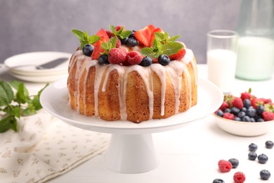 Photo of Delicious bundt cake with berries, glaze and mint on white wooden table against grey background, closeup