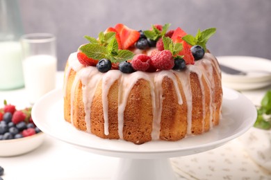 Photo of Delicious bundt cake with berries, glaze and mint on white table against grey background, closeup