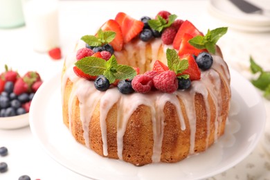 Photo of Delicious bundt cake with berries, glaze and mint on white table, closeup