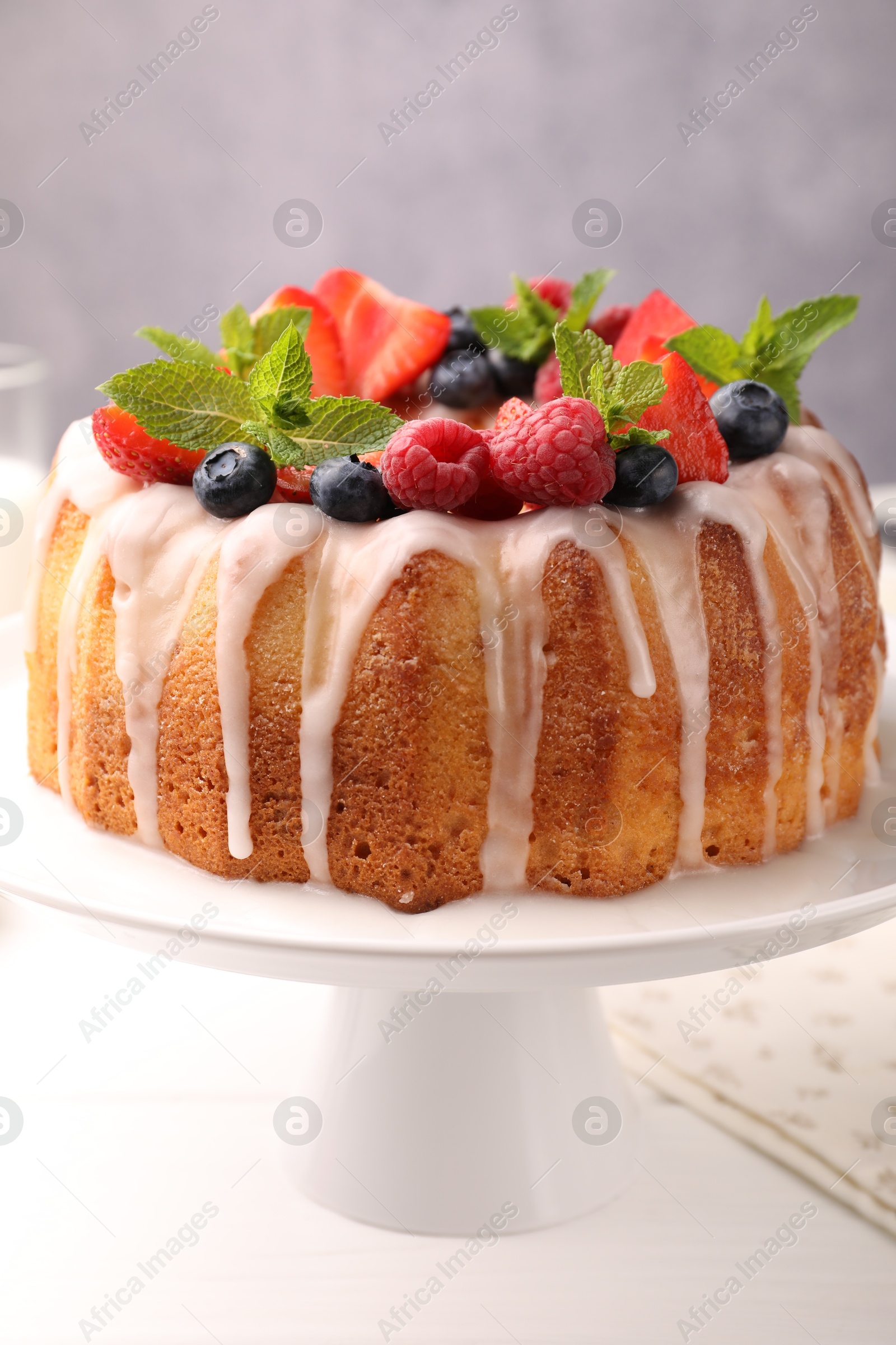 Photo of Delicious bundt cake with berries, glaze and mint on white wooden table against grey background, closeup