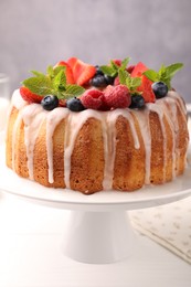 Photo of Delicious bundt cake with berries, glaze and mint on white wooden table against grey background, closeup