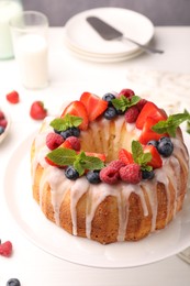 Photo of Delicious bundt cake with berries, glaze and mint on white table against grey background, closeup