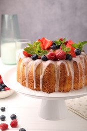 Photo of Delicious bundt cake with berries, glaze and mint on white wooden table against grey background, closeup