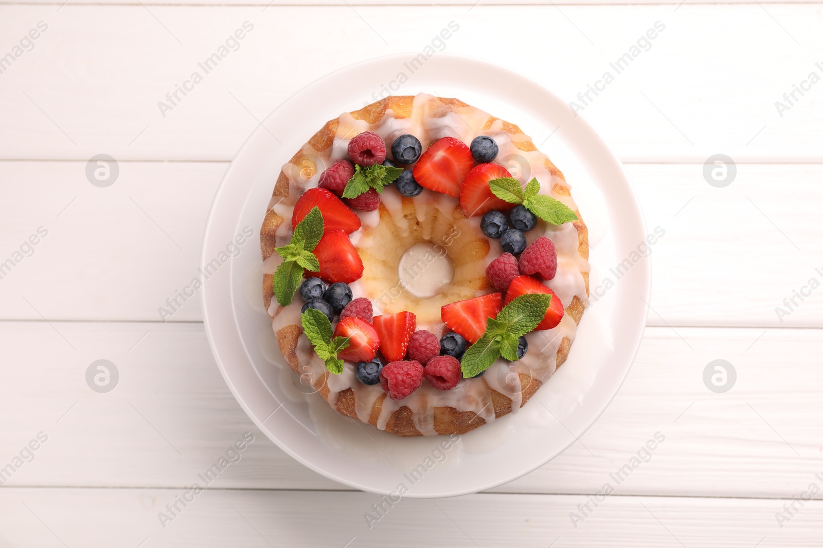 Delicious bundt cake with berries, glaze and mint on white wooden table, top view Photo of Delicious bundt cake with berries, glaze and mint on white wooden table, top view