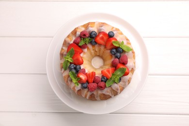 Photo of Delicious bundt cake with berries, glaze and mint on white wooden table, top view
