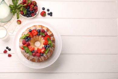 Photo of Delicious bundt cake with berries, glaze and mint on white wooden table, flat lay. Space for text