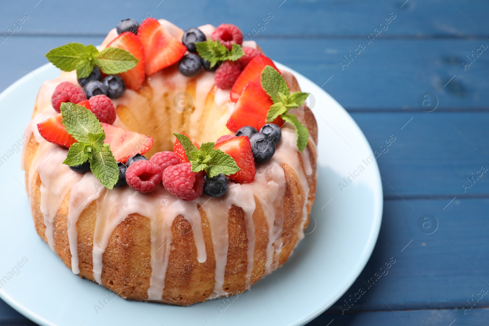 Delicious bundt cake with berries, glaze and mint on blue wooden table, closeup Photo of Delicious bundt cake with berries, glaze and mint on blue wooden table, closeup
